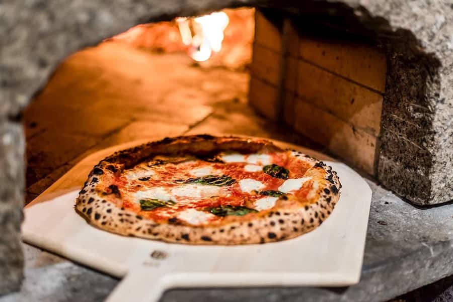 Produktbild einer Pizza Margherita, die aus dem Holzkohlenofen geholt wird.